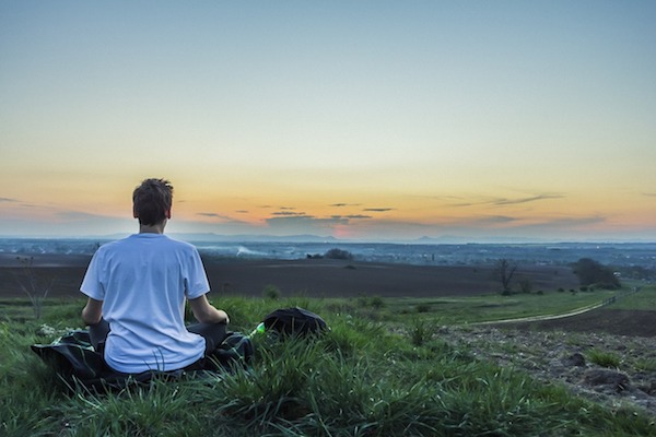 A man sitting on the ground in front of a sunset.