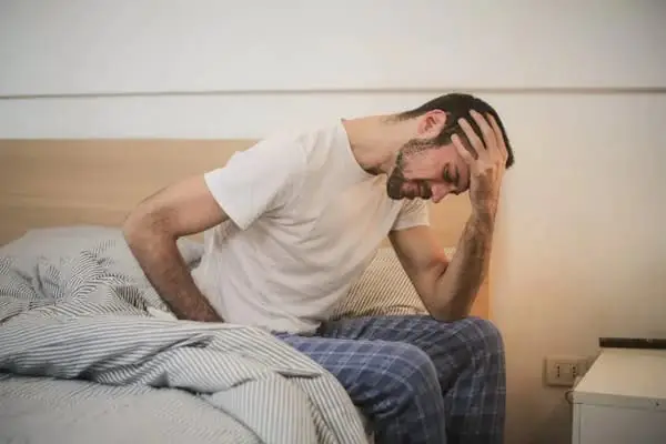 A man sitting on the bed with his head in his hand.