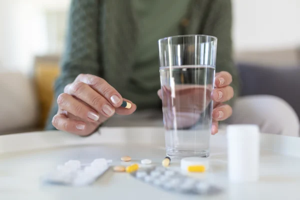 A person holding a pill and drinking water.